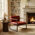 Red leather armchair with walnut sled base beside wooden side table, lamp, fireplace, and bookshelf
