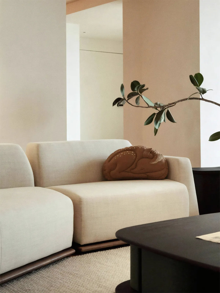 Close-up of Kyoto modular sofa with cream boucle upholstery and brown organic shaped pillow in a minimalist setting.