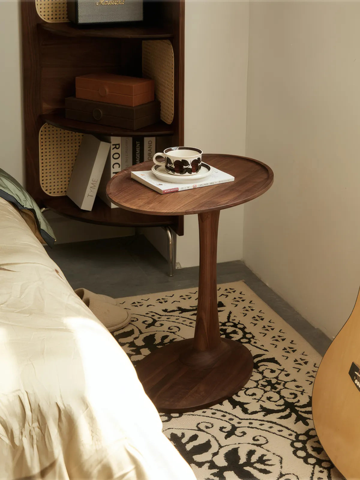 The Orbit solid black walnut side table by Walnutry, featuring an oval top and pedestal base, styled with books and coffee in a cozy reading nook.