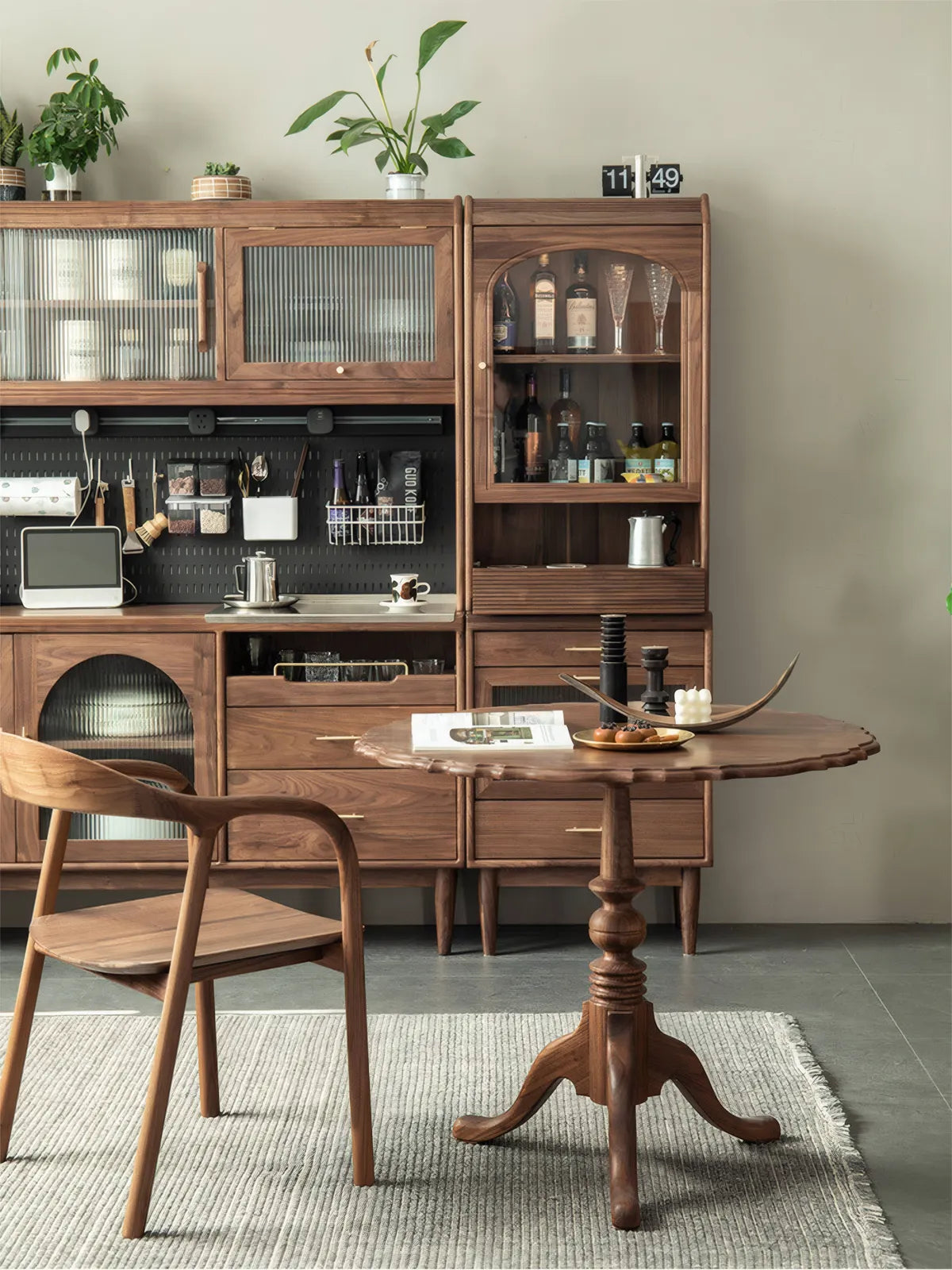 Full view of solid walnut scalloped pedestal table in a dining room with matching walnut hutch and pegboard wall.