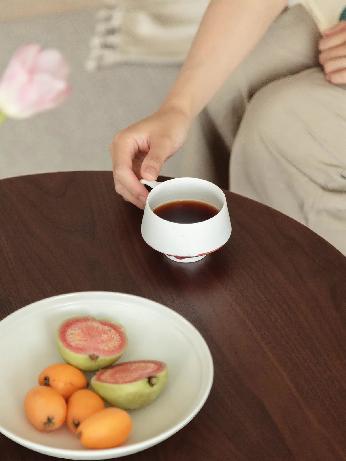 Close up of hand placing coffee cup on Cumberland solid walnut round side table, showing smooth satin finish.