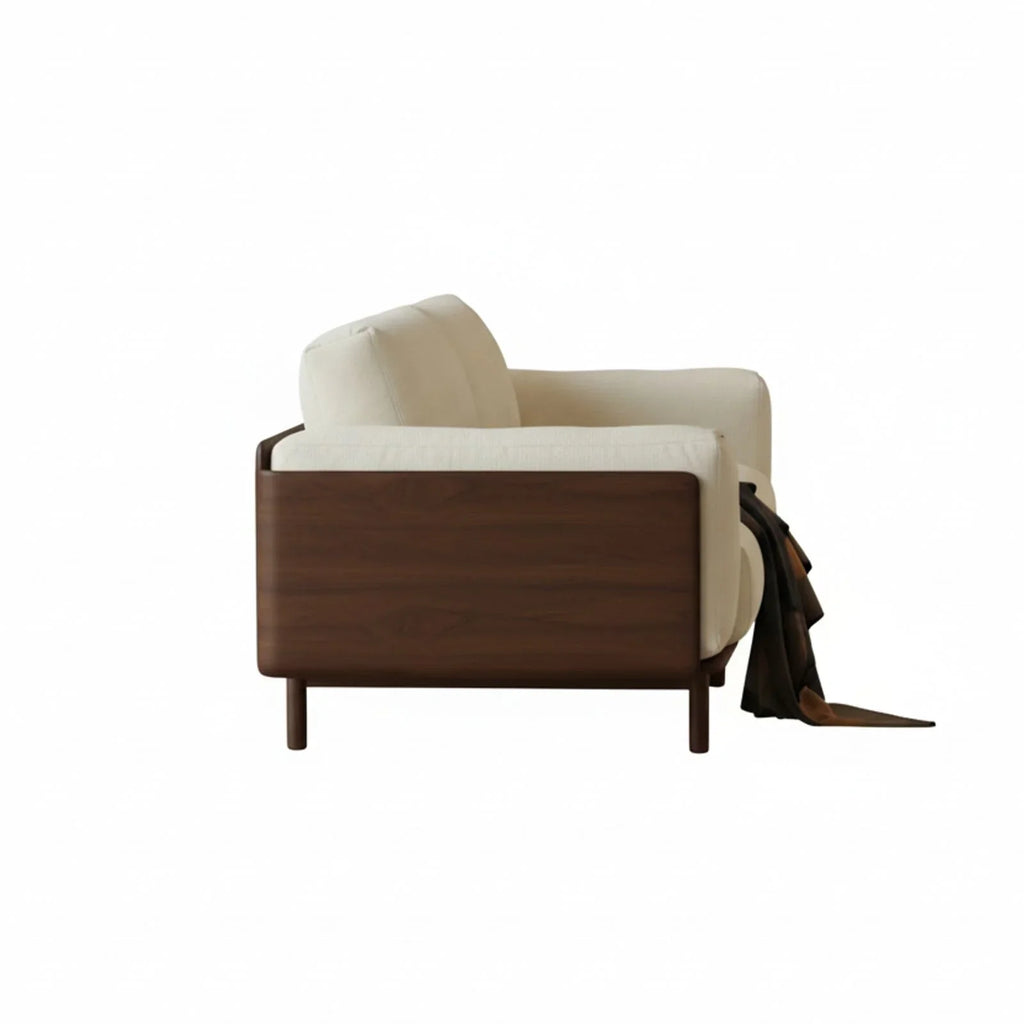 Side view of modern solid walnut sofa with cream fabric upholstery and draped dark brown throw