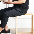 Person sitting on minimalist light wood bench wearing black pants and black sneakers reading a book