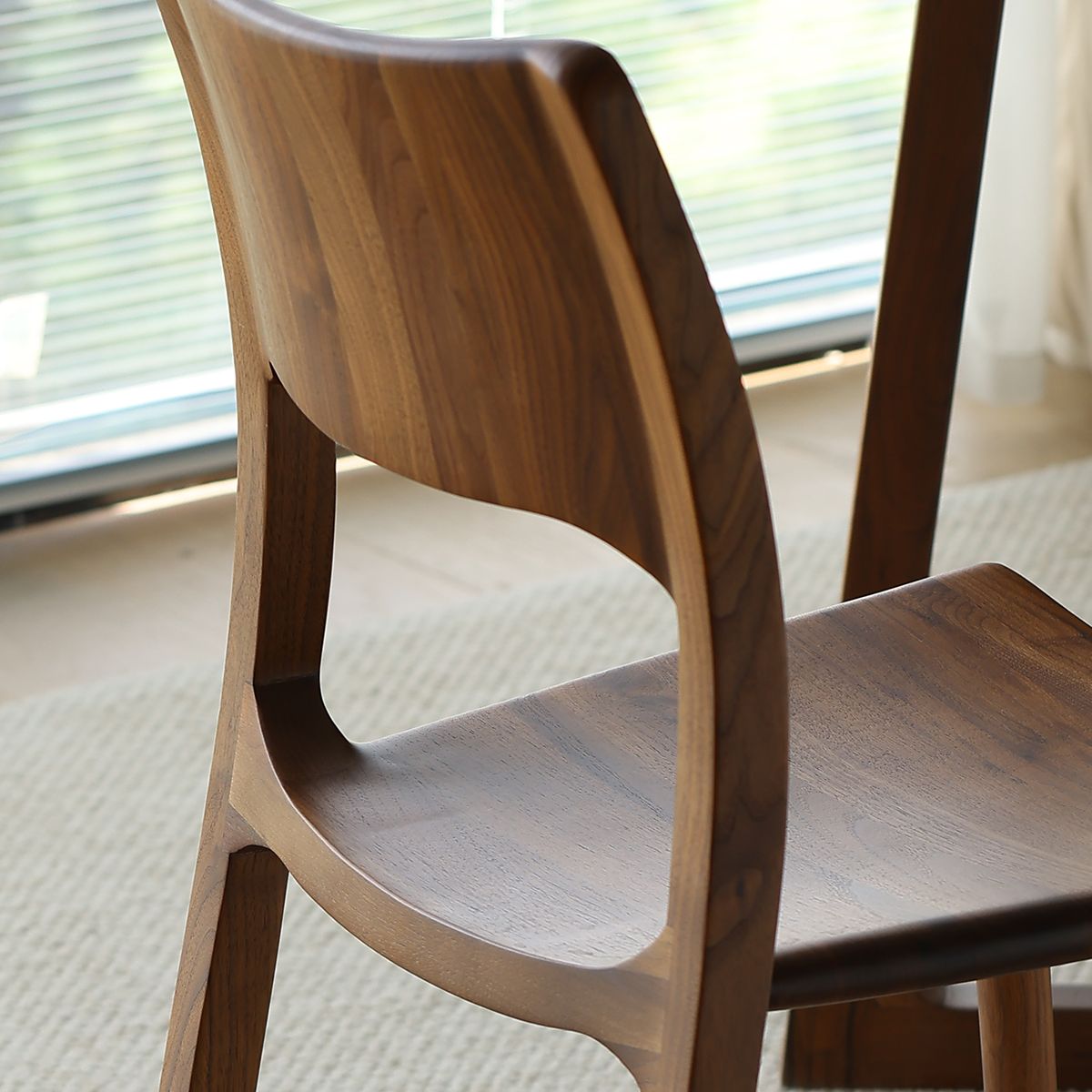 Back view of a solid wood dining chair with curved backrest in natural light