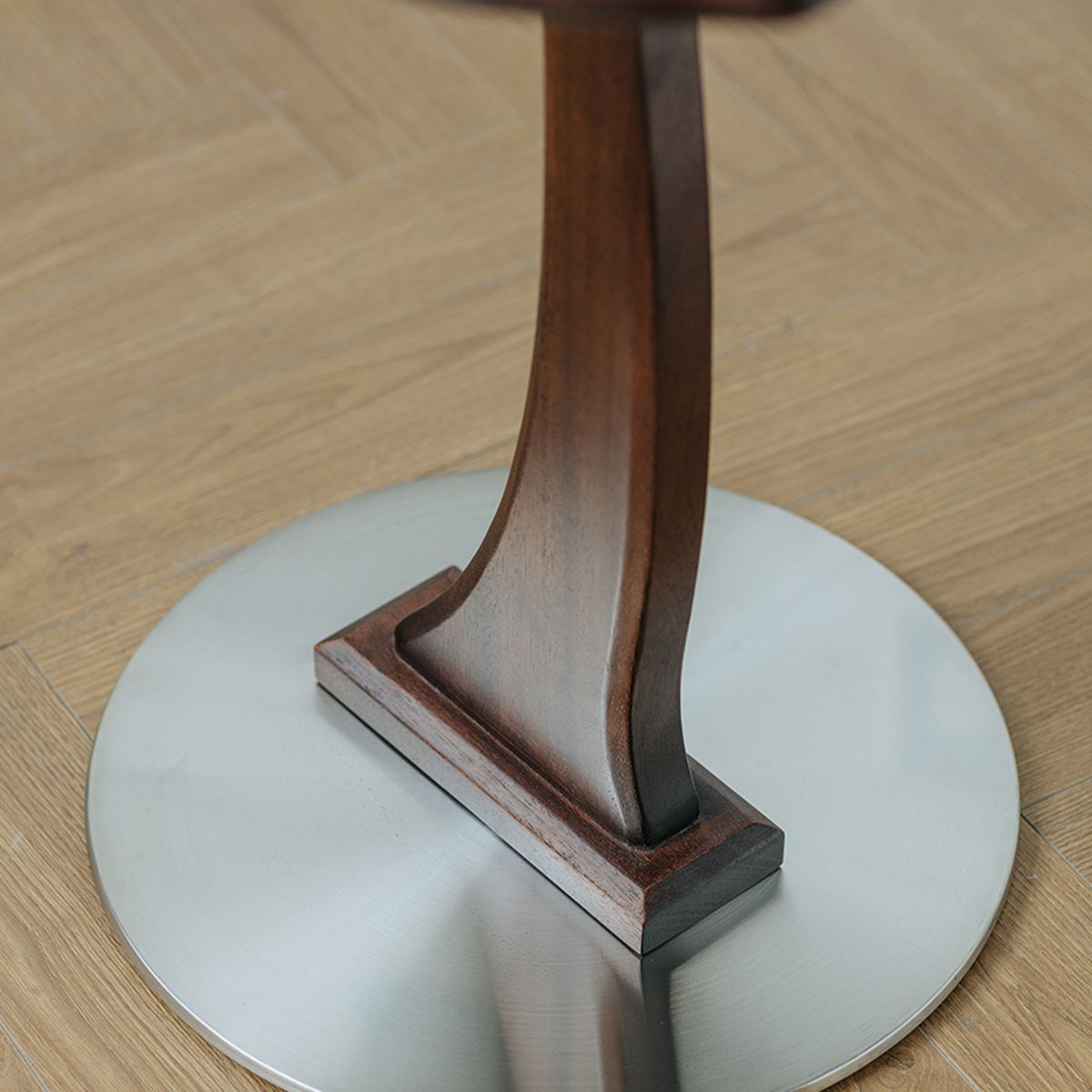 Close-up of carved solid wood table leg base on round metal floor plate, wood flooring background
