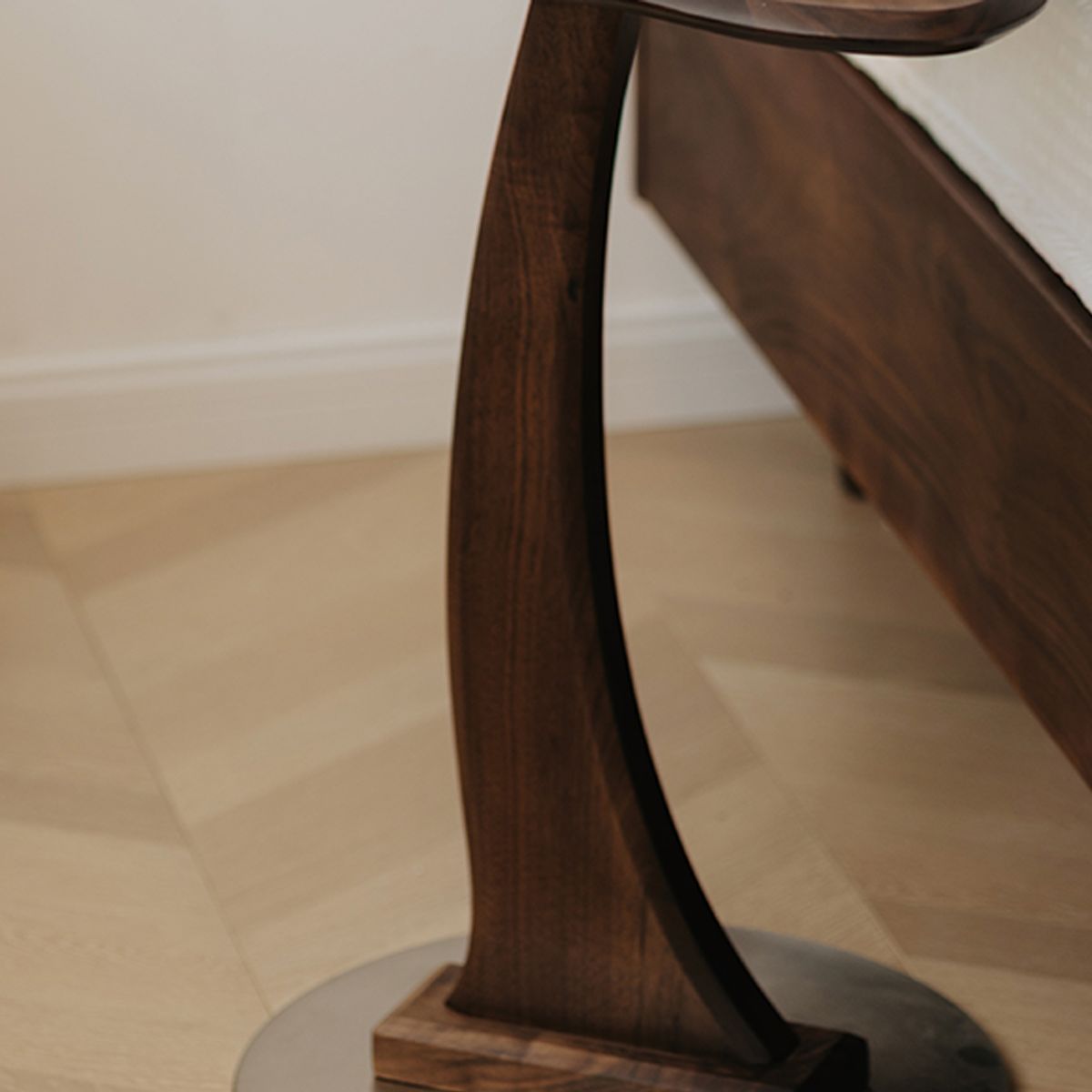 Close-up of dark solid wood end table leg with carved curved design on light hardwood floor