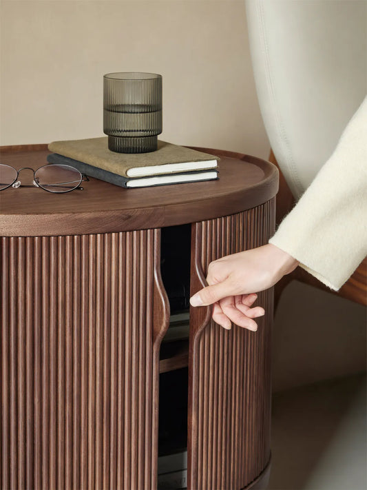 Hand sliding open the smooth tambour door of the Suiseki Oval Nightstand to reveal internal storage space.