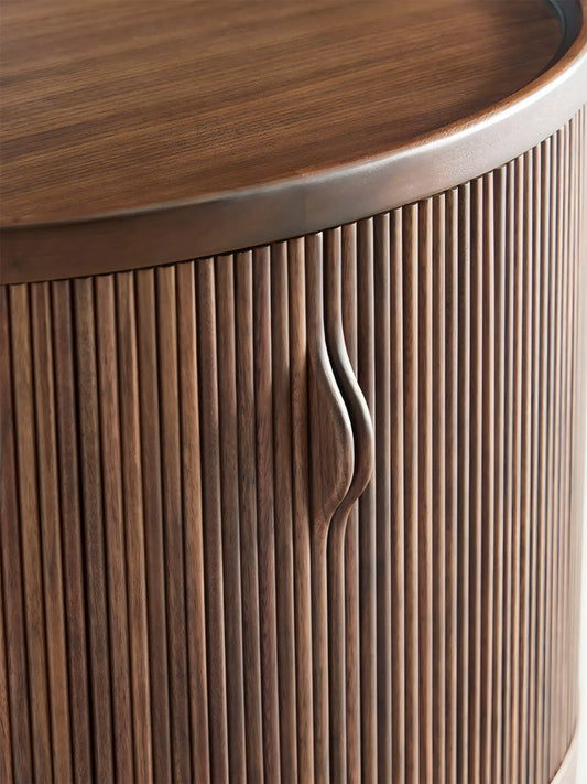 Close-up of Suiseki Oval Nightstand featuring solid black walnut wood grain and a sculpted handle integrated into the fluted tambour door.