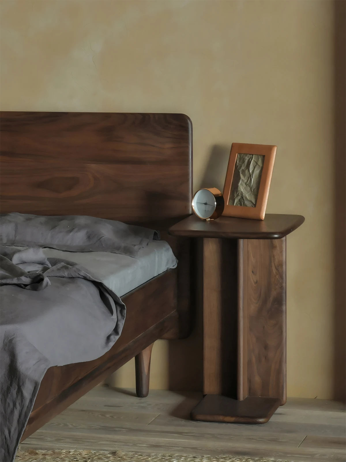 Solid walnut Suiseki C-table placed next to a wooden bed in a Japandi style bedroom, acting as a minimalist nightstand.