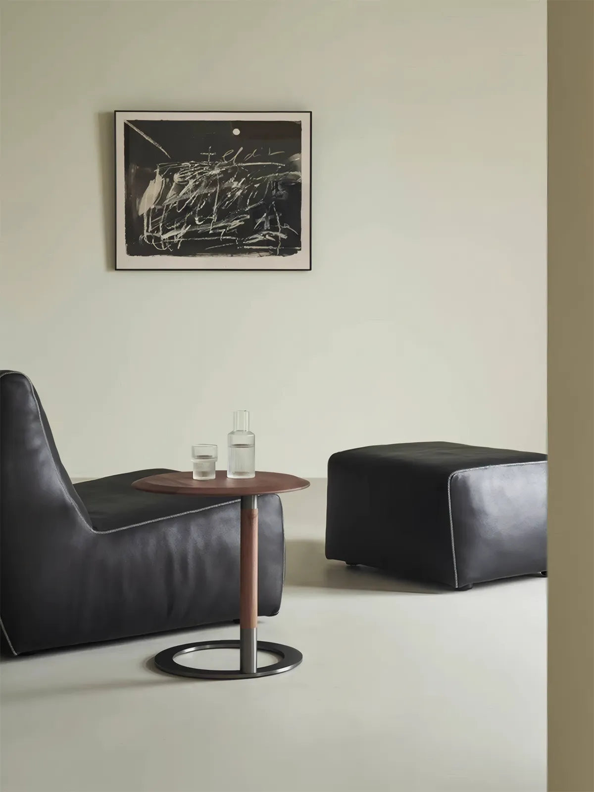 Walnutry Suiseki solid walnut C-table positioned next to a black leather lounge chair with a glass water bottle on top, showcasing modern living room styling.