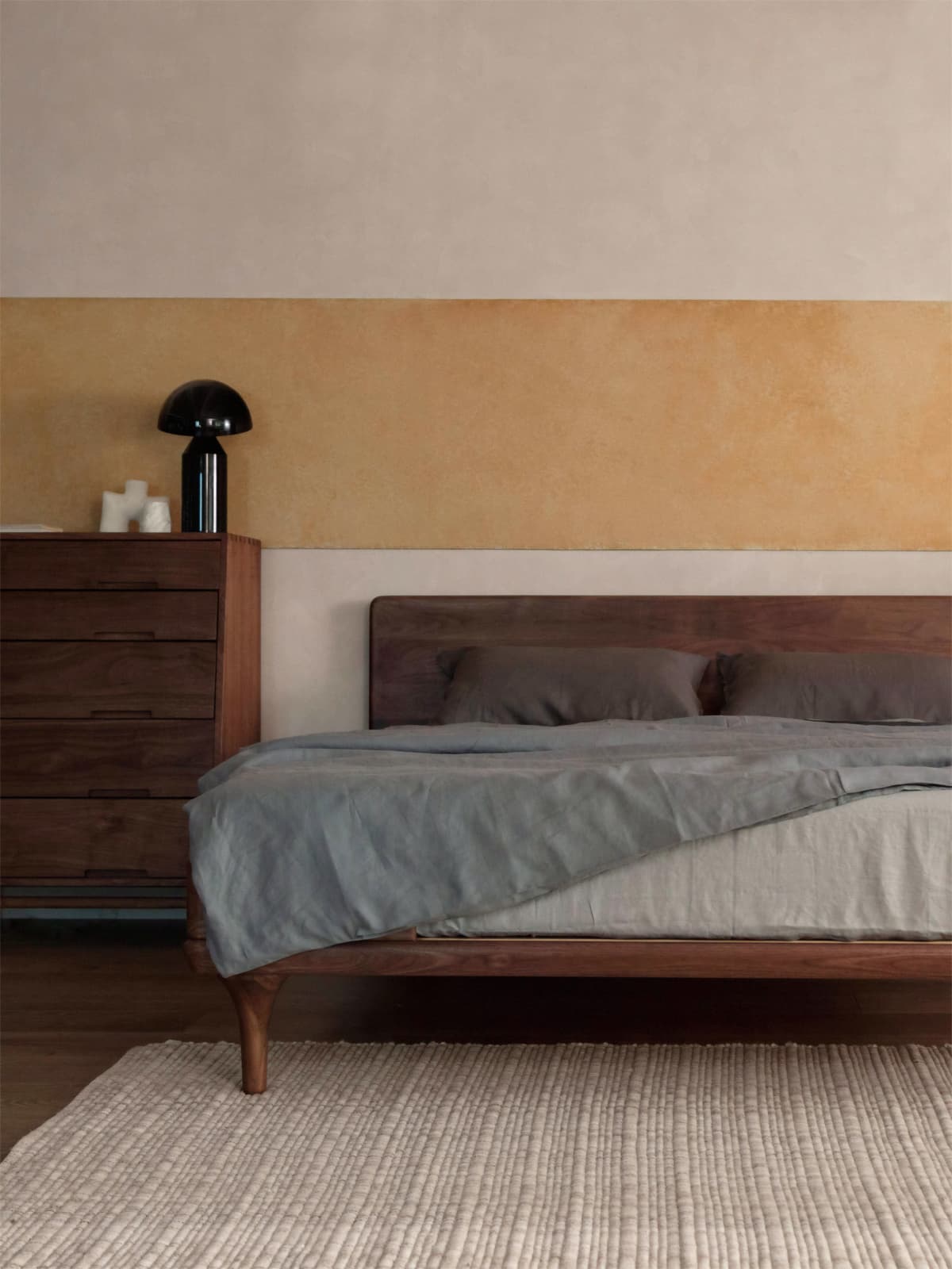 The Estate Bed Frame styled in a warm, modern bedroom interior with a matching walnut dresser and textured rug.