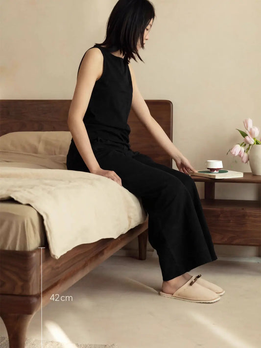 Lifestyle shot showing the comfortable 42cm seating height of The Estate Bed Frame, featuring solid wood legs.