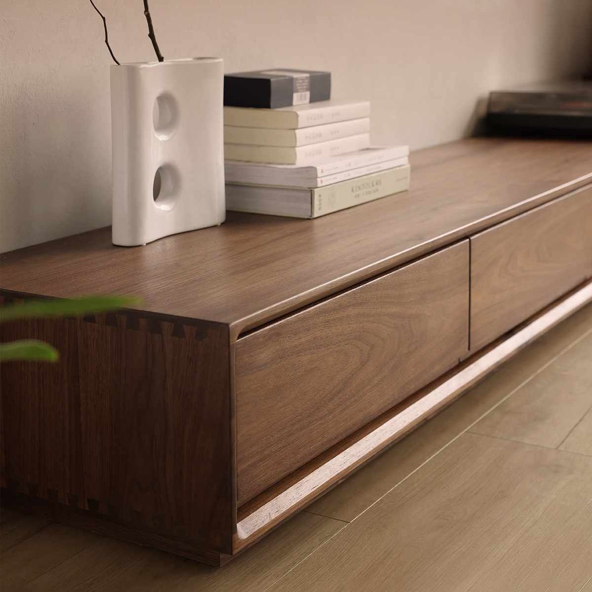 Side profile of ultra low walnut wood TV cabinet with decorative white vase and stacked books