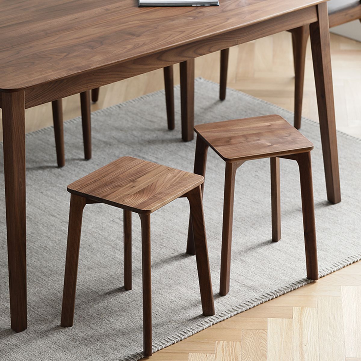 Two versatile wooden stools used as side tables on a gray rug under a wooden dining table