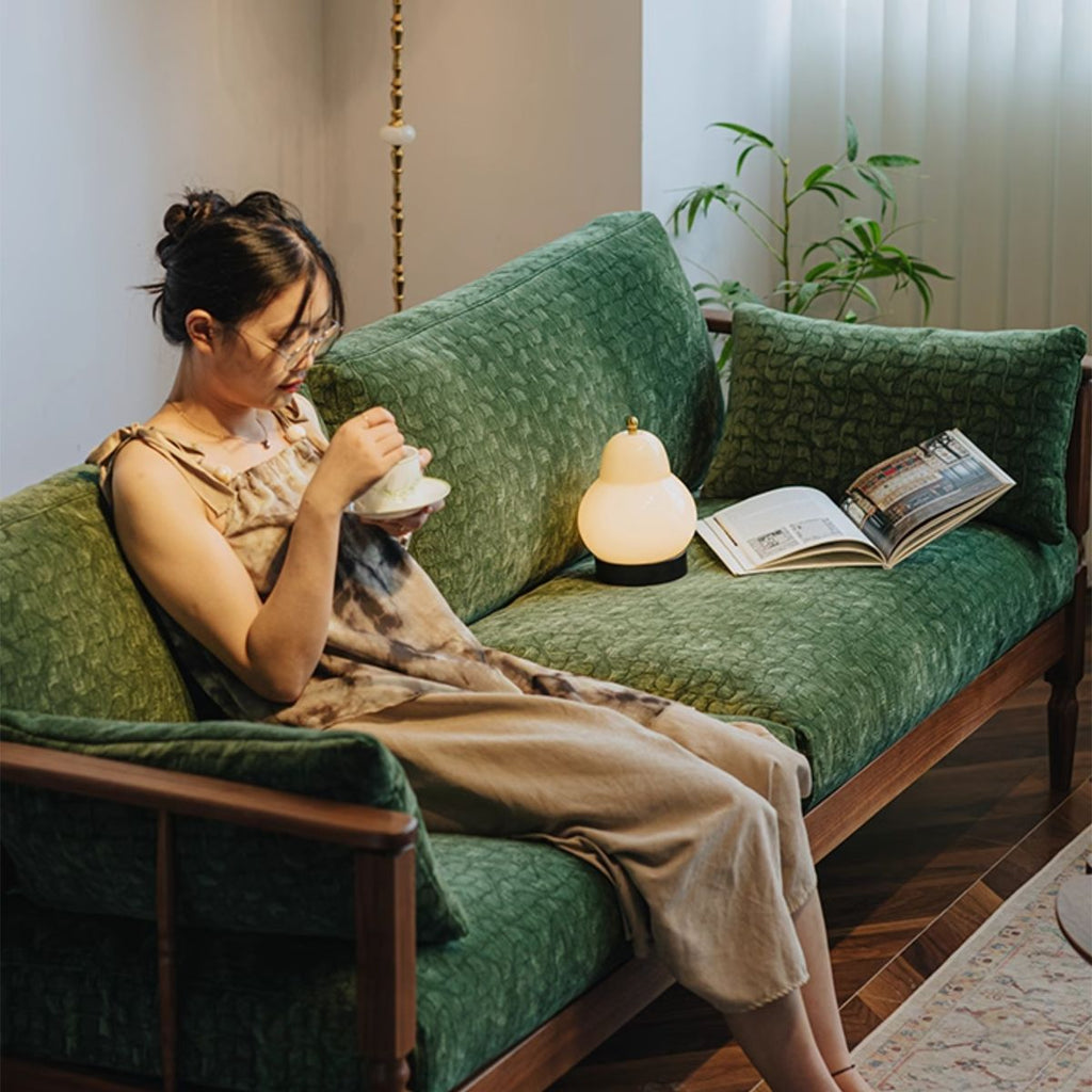 Woman drinking tea on vintage green velvet couch with wooden frame in cozy living room