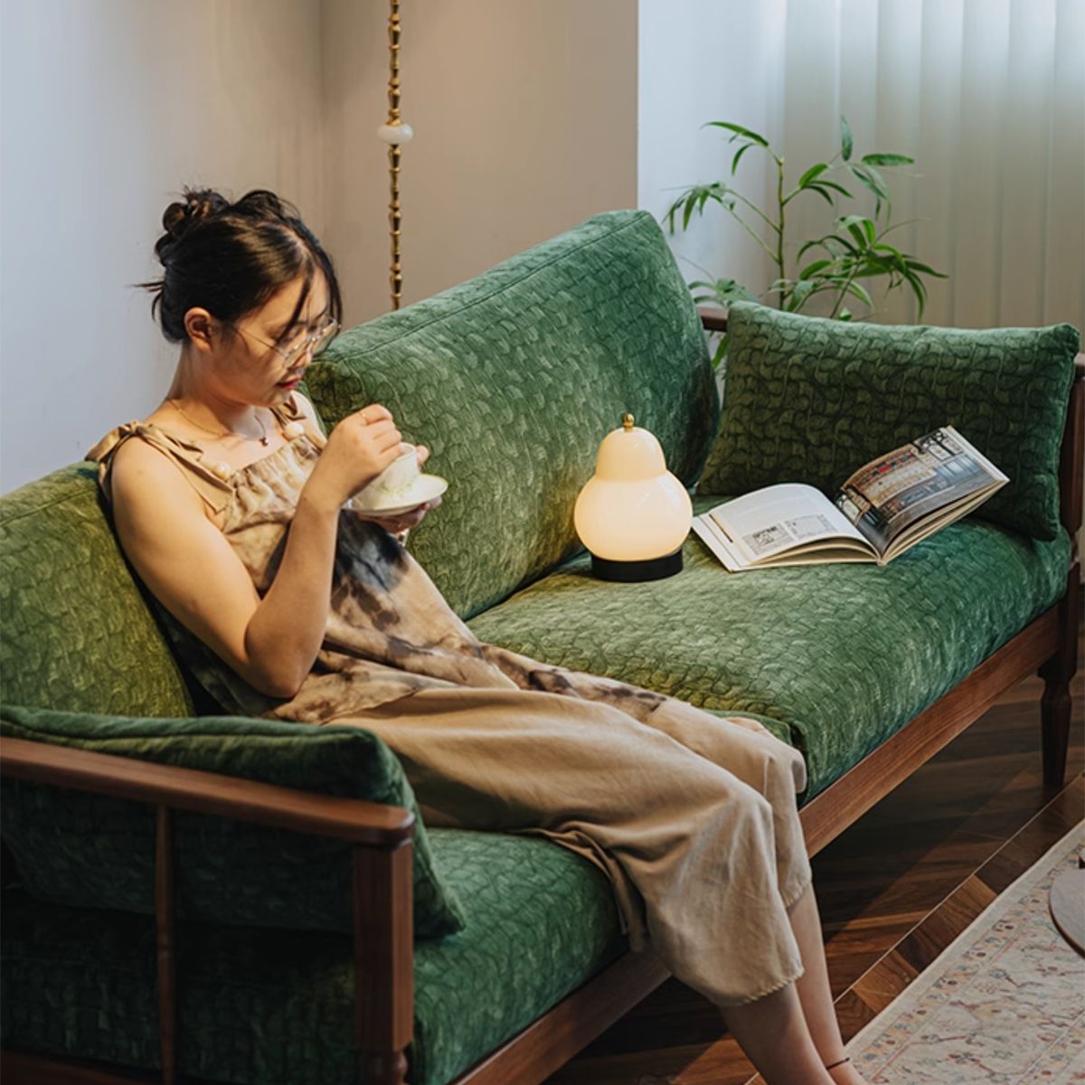 Woman drinking tea on vintage green velvet couch with wooden frame in cozy living room