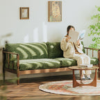Vintage style living room with walnut frame green couch, round wooden coffee table, rug, and woman reading a book