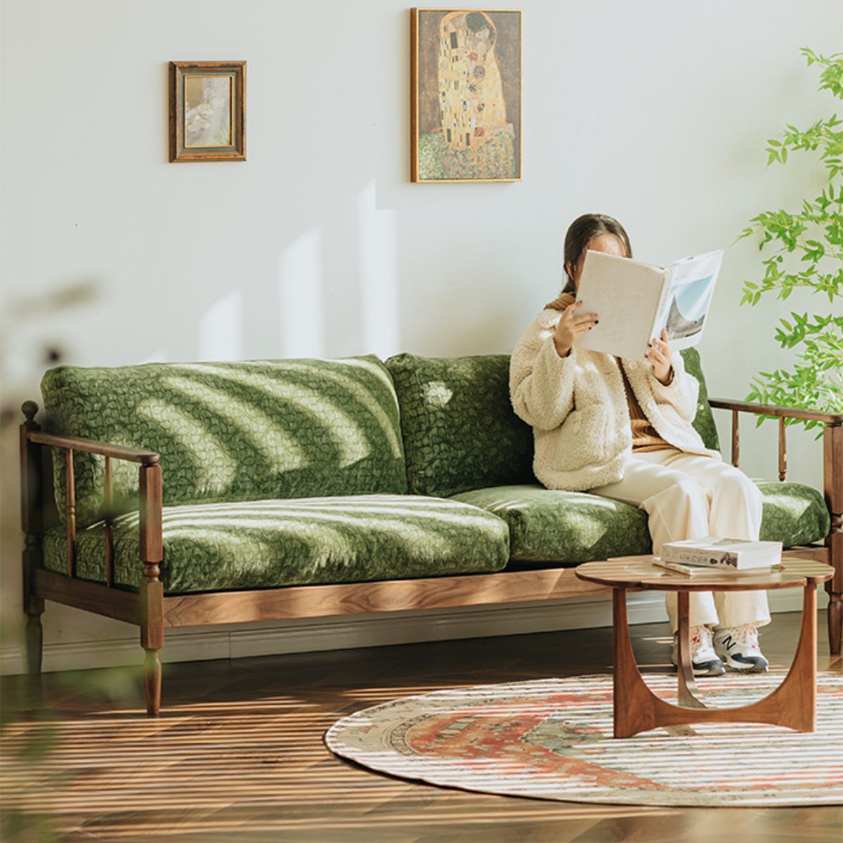 Vintage style living room with walnut frame green couch, round wooden coffee table, rug, and woman reading a book