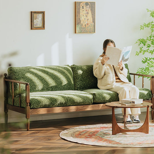 Vintage style living room with walnut frame green couch, round wooden coffee table, rug, and woman reading a book