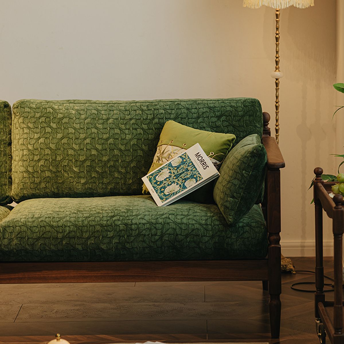 Vintage-style green velvet sofa with decorative cushions and a Morris book in a cozy living room