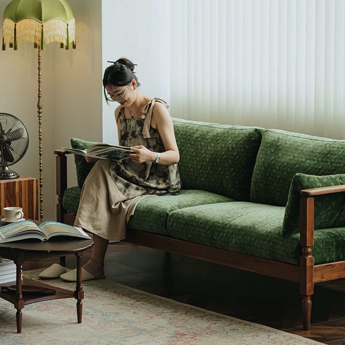 Woman reading on vintage green upholstered walnut couch in cozy living room with wooden table and floor lamp