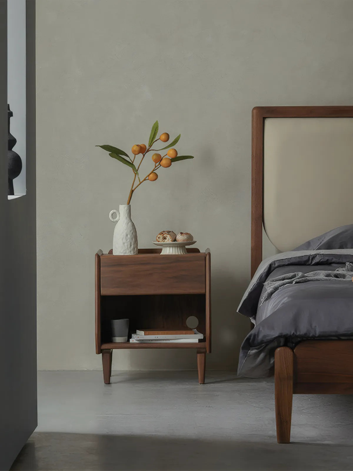 Angled view of walnut bedside table showing solid wood construction and sleek organic modern silhouette.