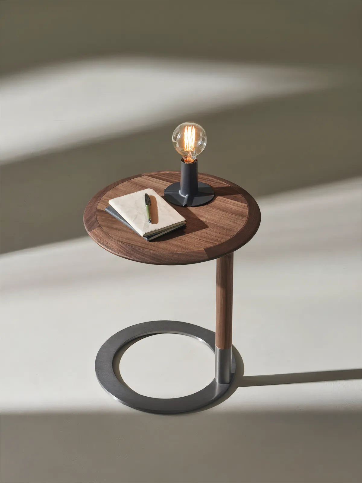 The Suiseki C-table styled with a modern industrial lamp and journal, demonstrating its use as a functional reading table.