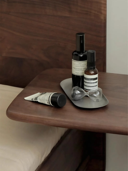 Close-up of North American Black Walnut wood grain on C-table surface, displaying luxury skincare bottles and hourglass decor.

