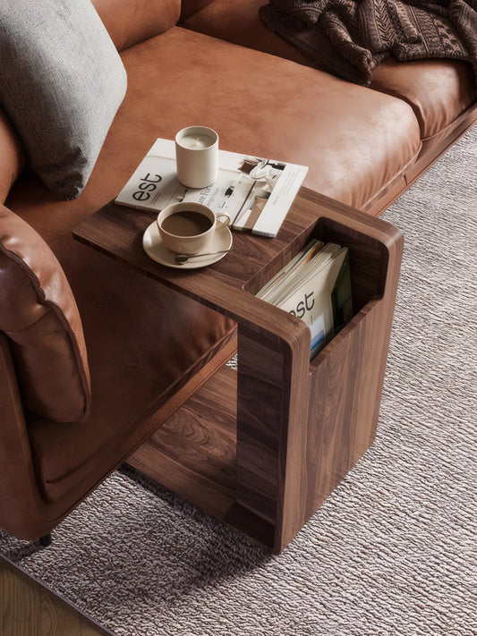 Solid walnut C-table with integrated magazine storage slot next to brown leather sofa.