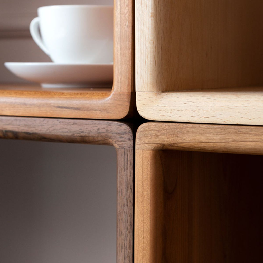 Close-up of four wooden cube shelves made of walnut, cherry, and poplar woods with smooth rounded edges and a white cup on a saucer