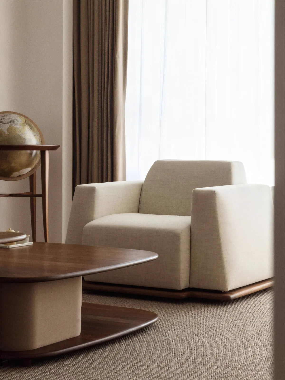 Walnutry Nara oversized walnut lounge chair in a cozy reading nook with a vintage globe and side table.