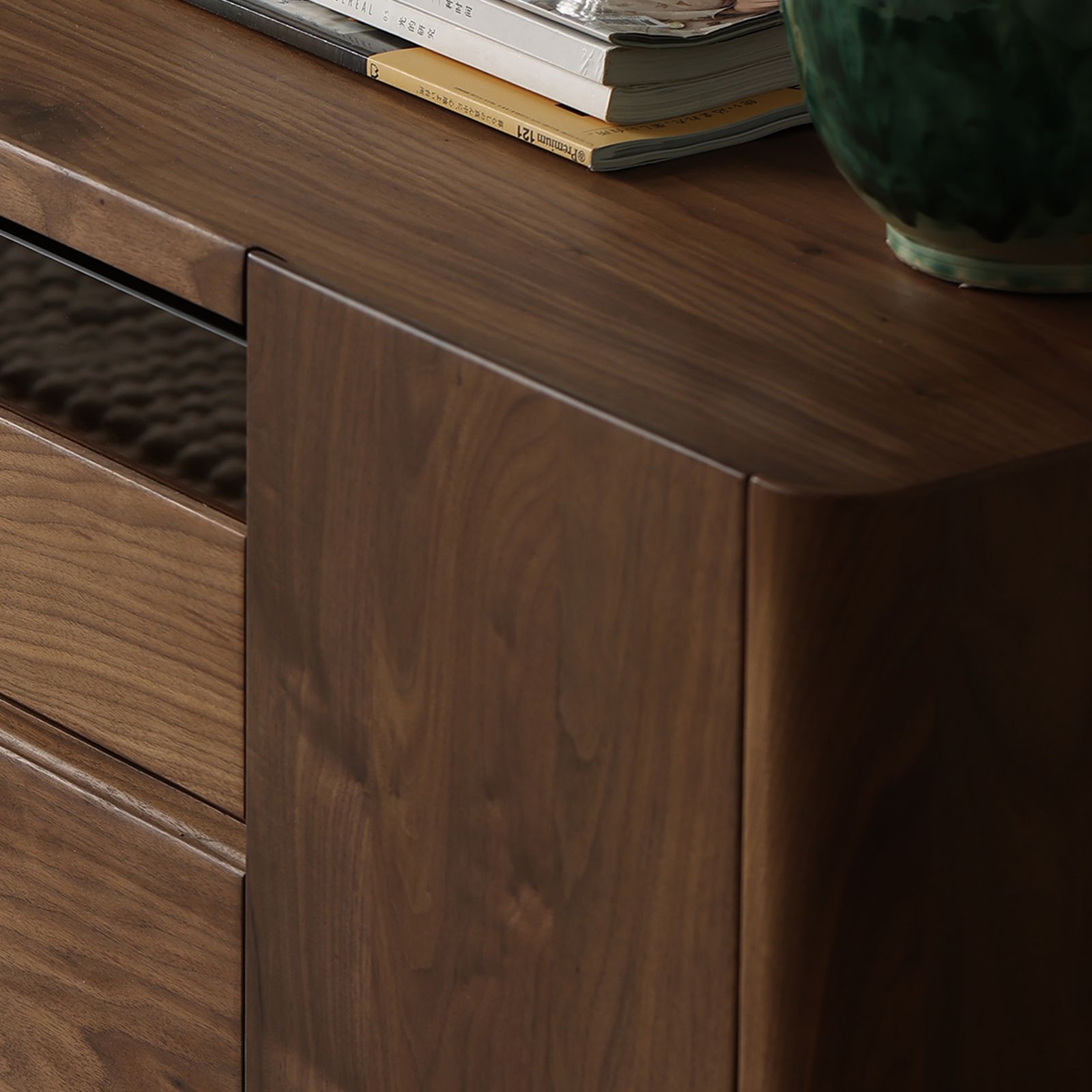 Side profile of walnut media cabinet with smooth finish, books, and ceramic vase on top