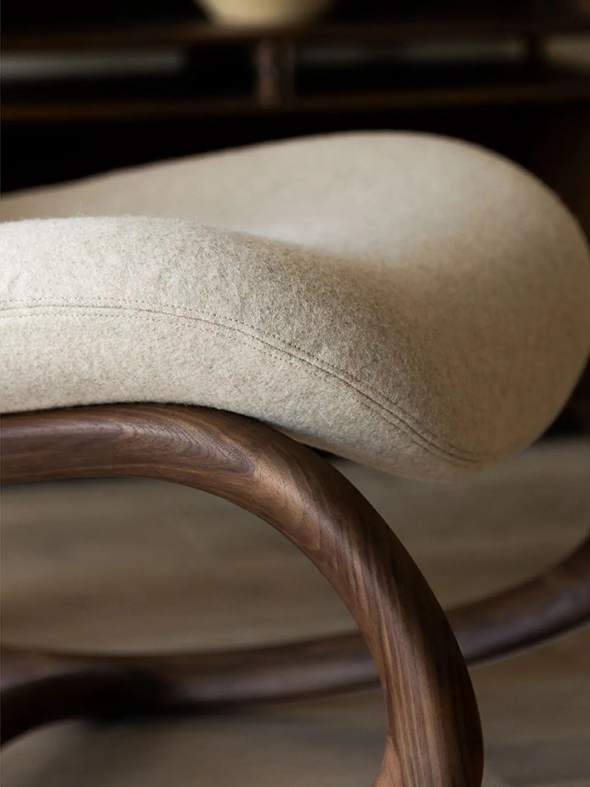 Close-up of solid black walnut armrest showcasing seamless organic joinery and oatmeal bouclé fabric texture.
