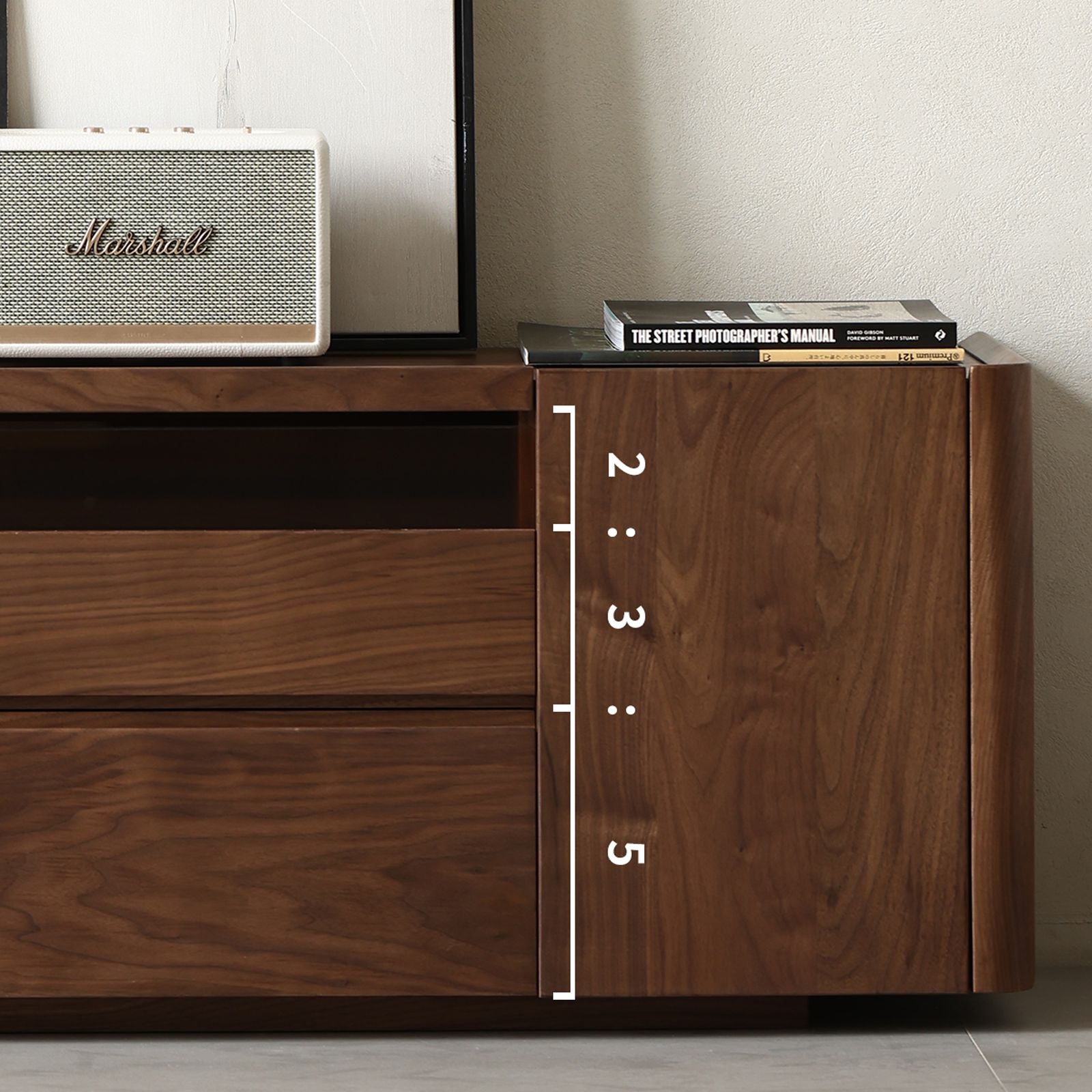 Close-up of walnut wood grain TV cabinet side with drawers, books, and Marshall speaker on top