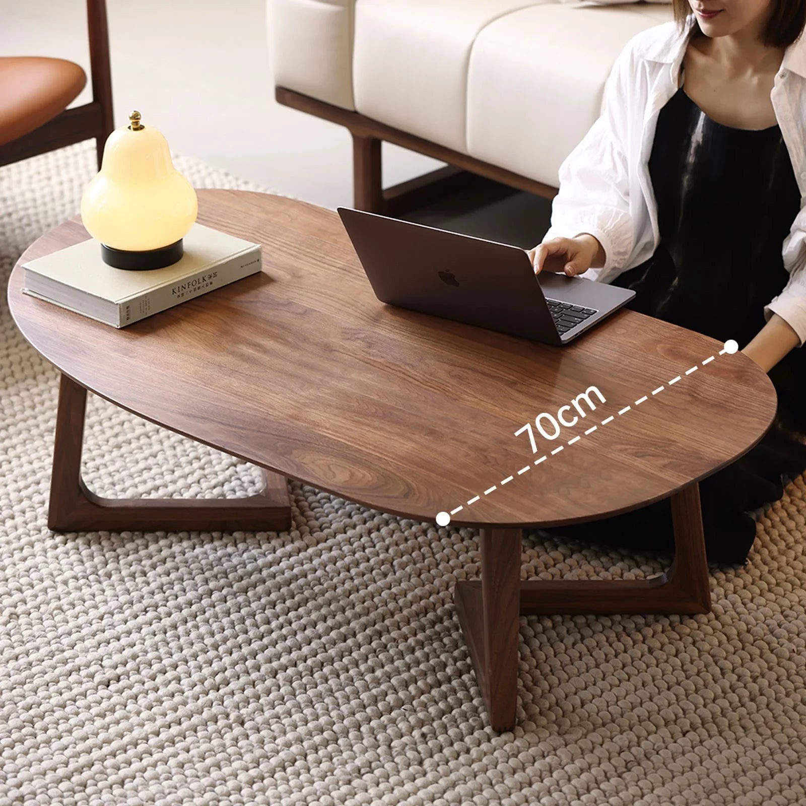 Oval walnut wood coffee table on textured carpet with lamp and person using laptop