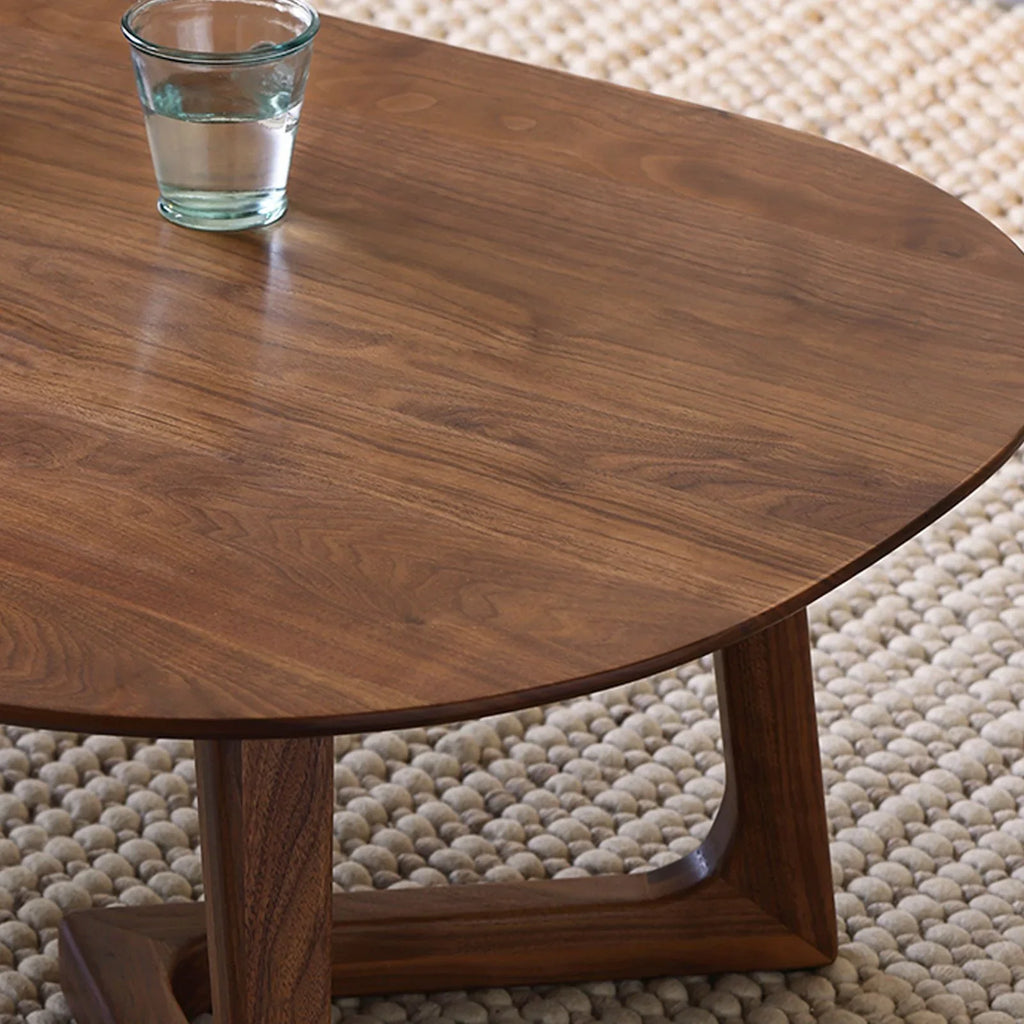 Close-up of walnut wood grain coffee table with glass of water on textured beige rug