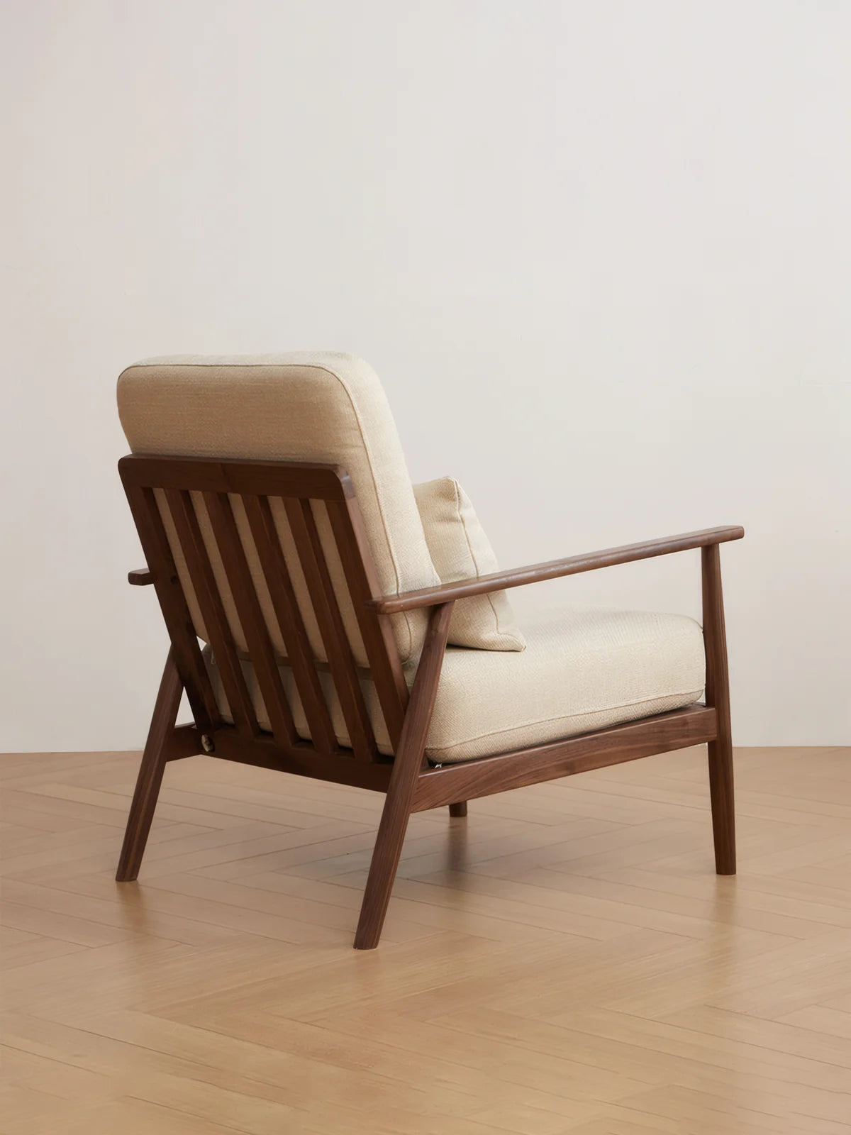 Walnutry Alden Armchair back view showing slatted walnut support frame, angled rear legs, and upholstered cushions in a clean modern interior