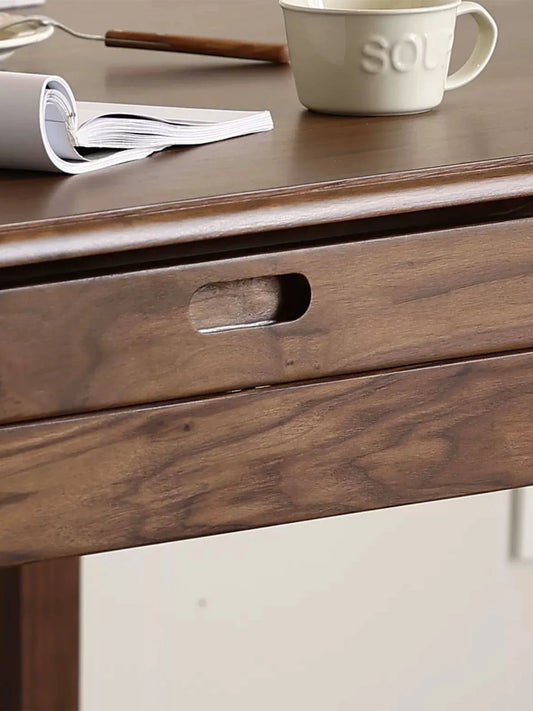 Close-up of the apron and recessed pull on a walnut extendable dining table, with a rolled magazine, a mug, and a small utensil on the tabletop.