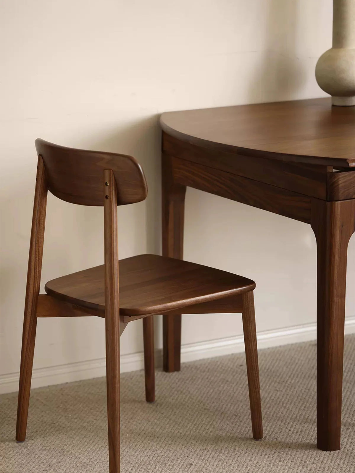 Side view of the walnut extendable dining table in its compact wall-side setup, paired with a matching wooden dining chair.