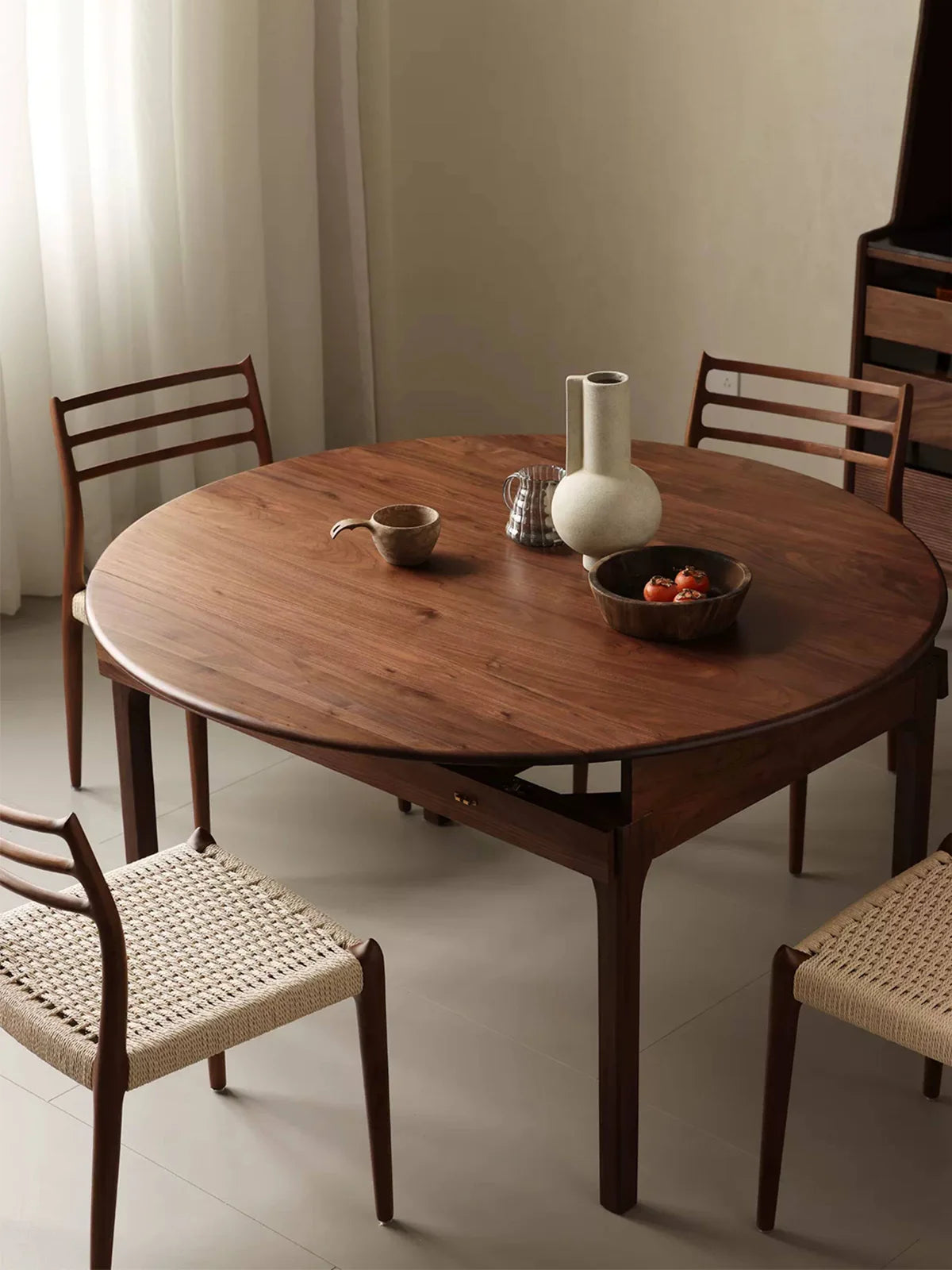 Full round view of the walnut dining table set with woven-seat chairs and simple tabletop decor, showing the expanded configuration.