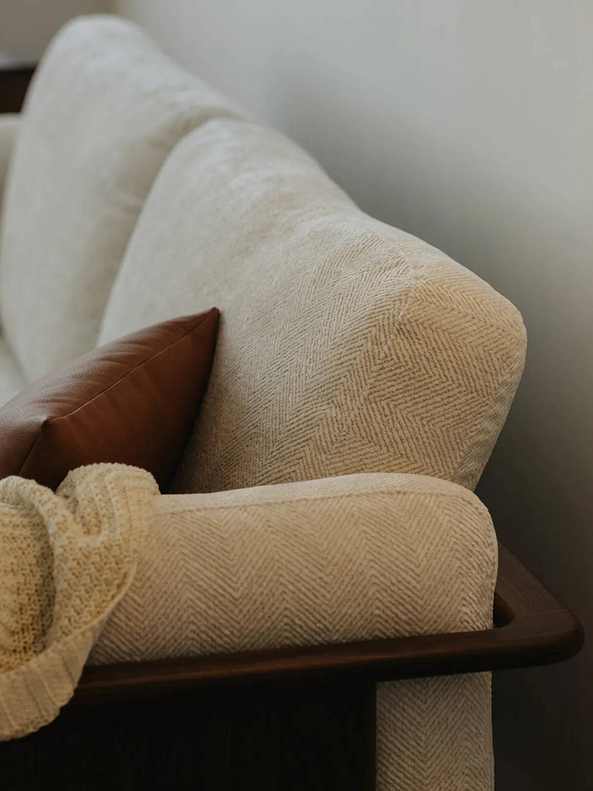 Detail of Alden Ridge sofa backrest and walnut arm rail in wheat upholstery with a leather accent pillow