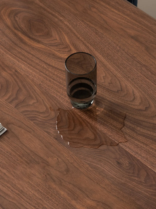 Water resting on the surface of the Auren solid walnut dining table, showing the protective hard wax oil finish.