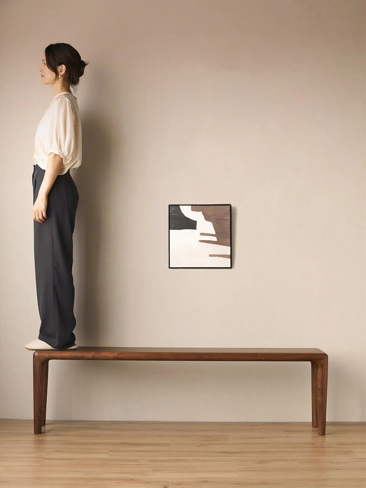 A woman standing on the Auren Walnut Bench to demonstrate strength, stability, and durable solid wood construction.