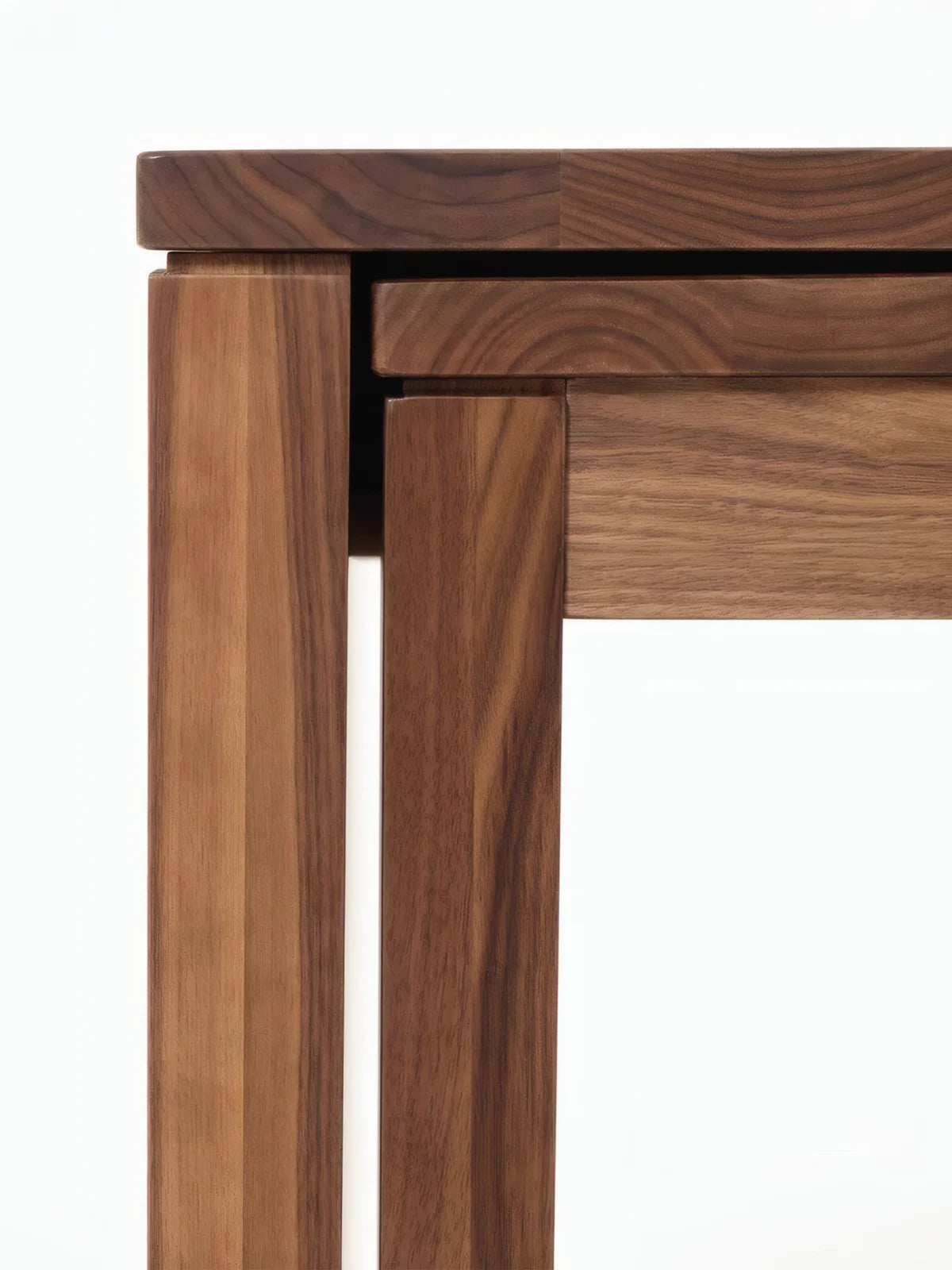 Close-up of the dining table corner showing the layered apron detail, square legs, and walnut joinery