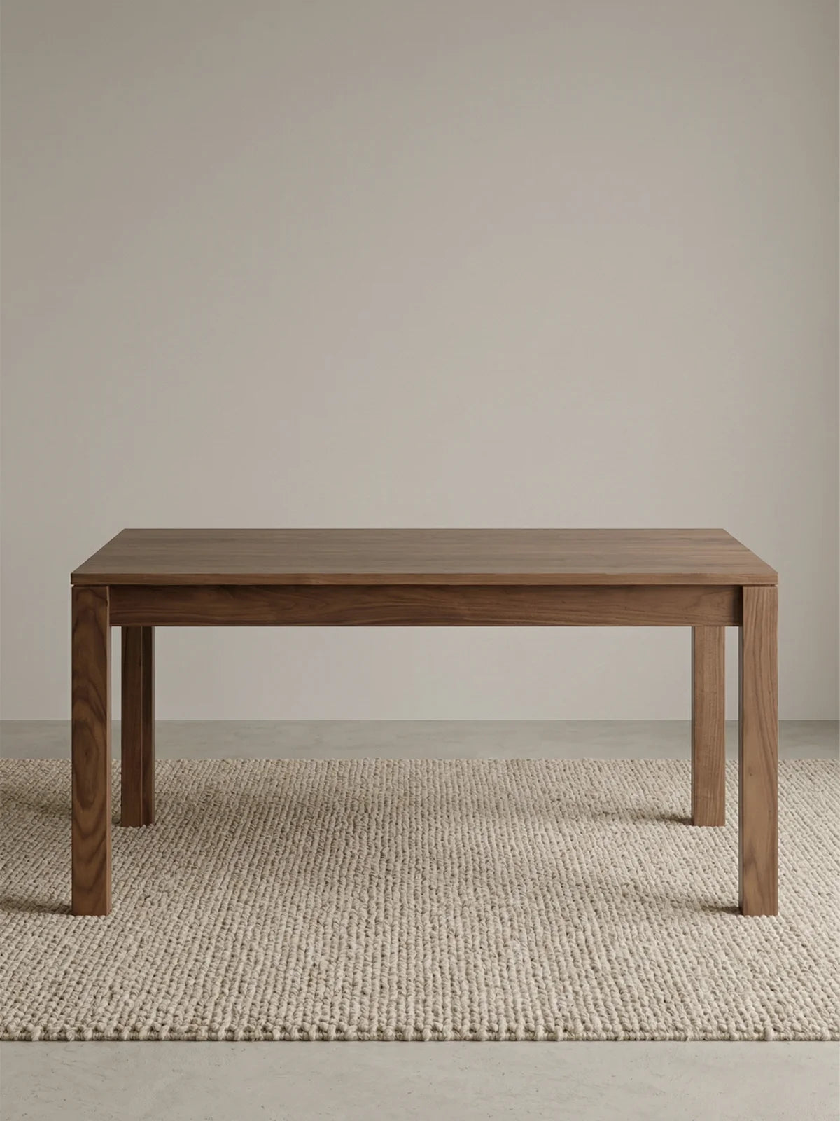 Studio view of the solid walnut dining table in closed form on a textured neutral rug