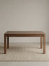 Studio view of the solid walnut dining table in closed form on a textured neutral rug