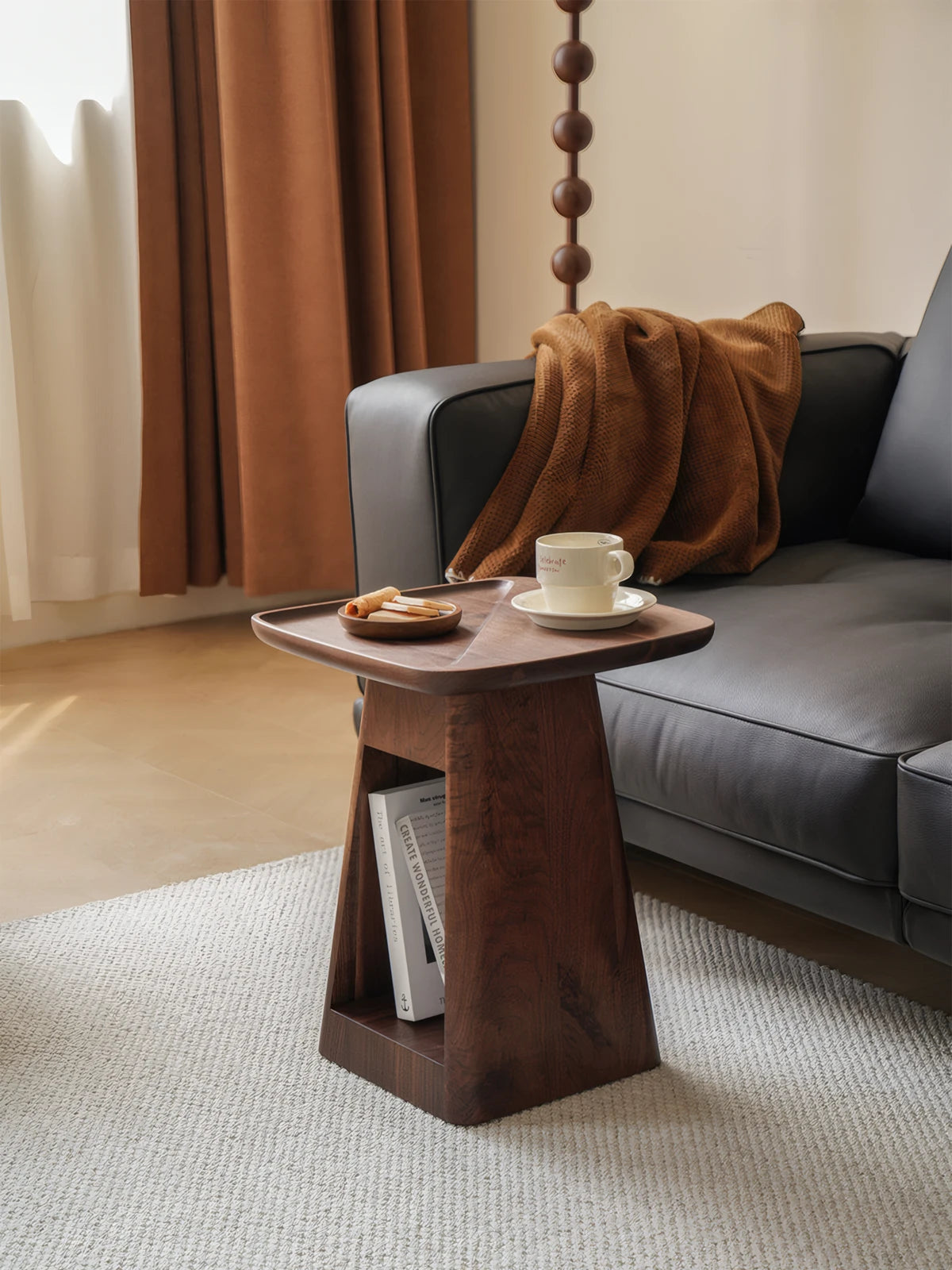 Walnutry Kurumi black walnut end table placed next to a modern dark leather sofa in a Japandi style living room.