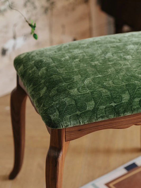 A close-up view of The Bourbon Vanity Stool showing the intricate embossed pattern on the plush green velvet upholstery.
