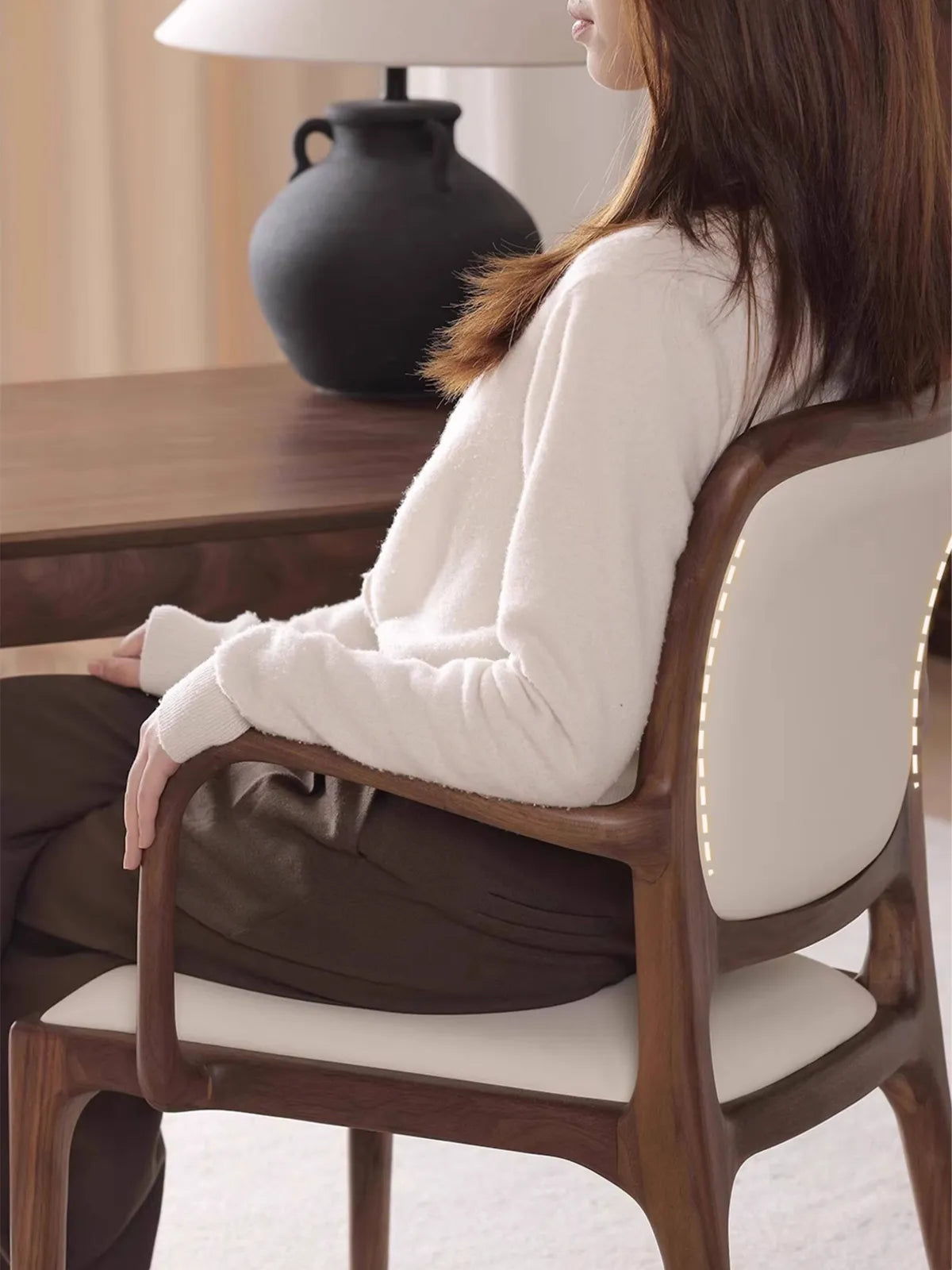Side view of a person seated in the Cael arm chair at a desk, showing armrest height and backrest support in use.