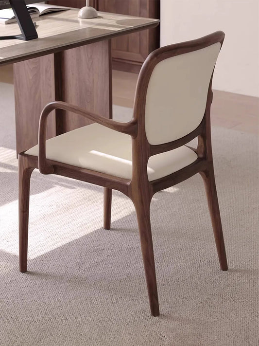 Rear three-quarter view of the Cael dining arm chair beside a desk, highlighting the continuous curved walnut back frame.